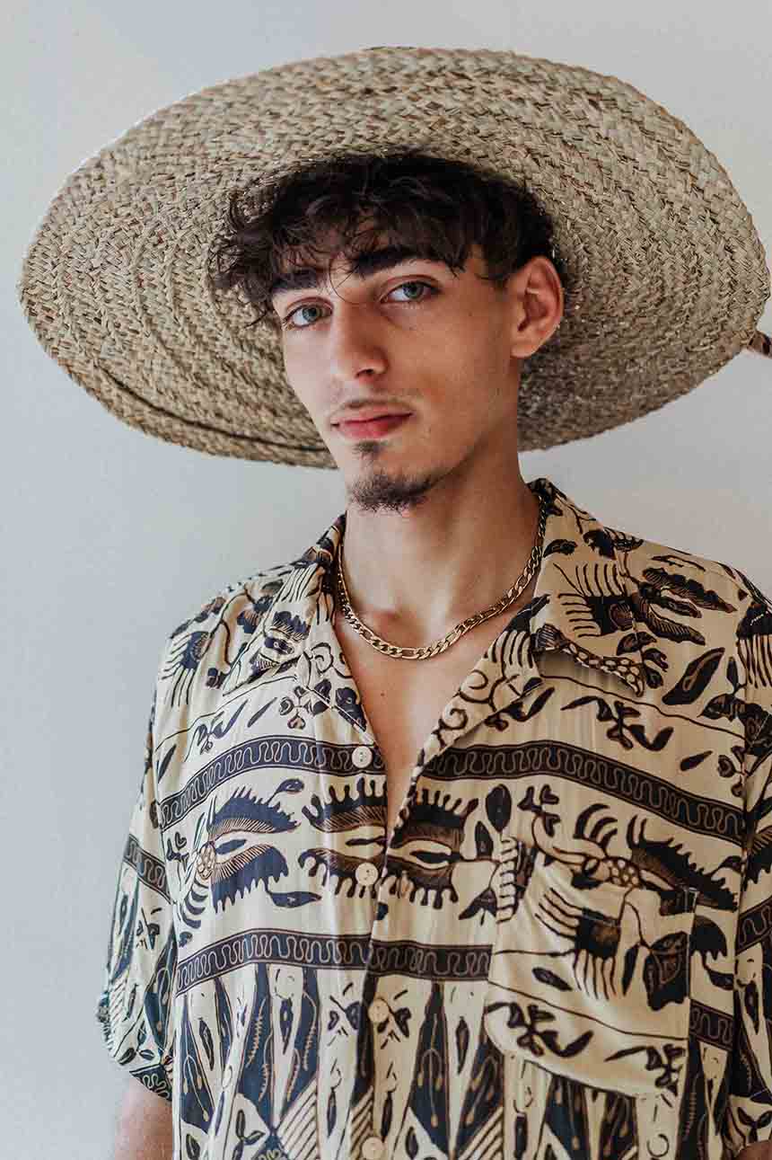 Man wearing a straw hat and patterned shirt against a plain background