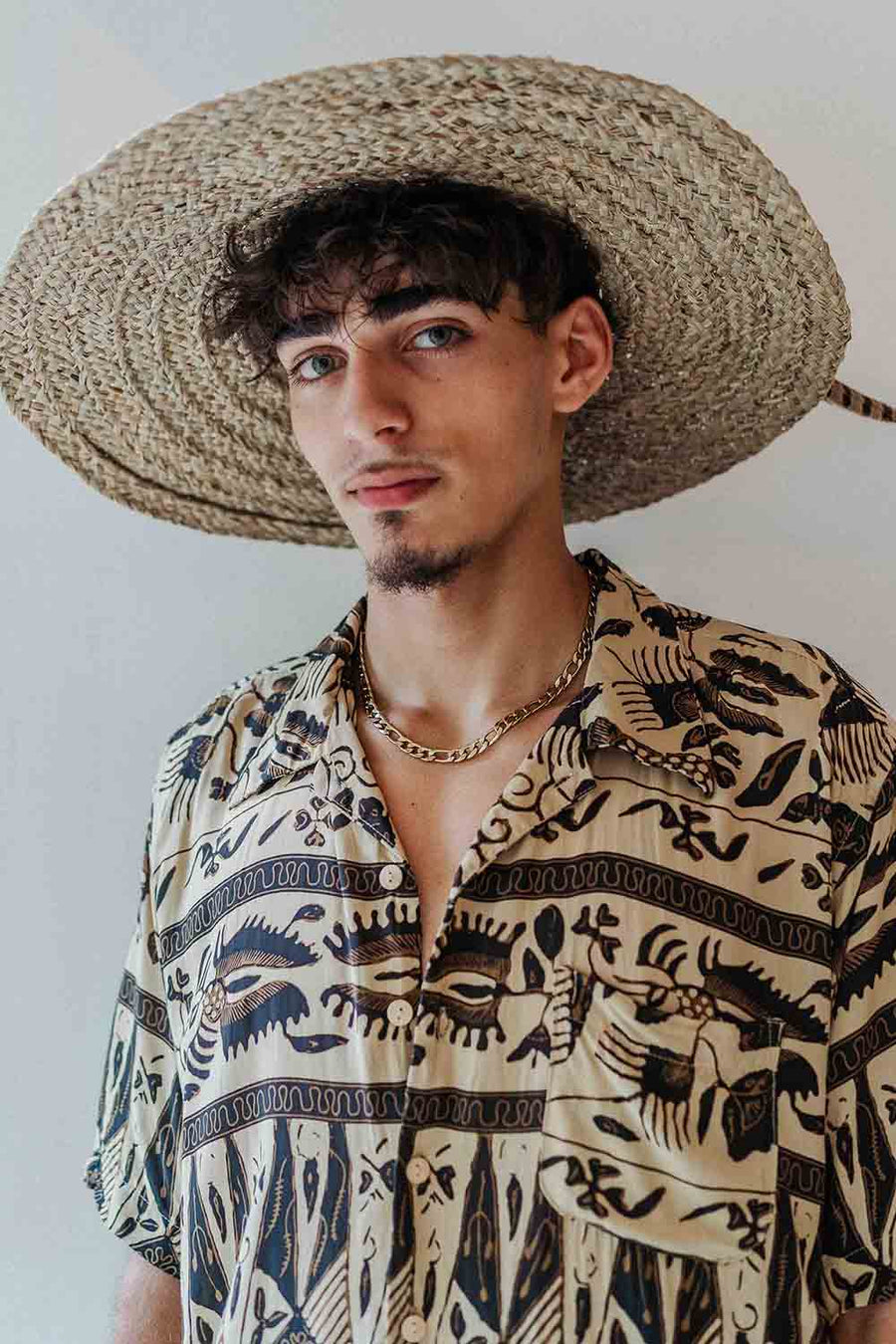 Man wearing a straw hat and patterned shirt against a plain background