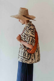 Person wearing a patterned shirt and straw hat with a brown bag against a white background