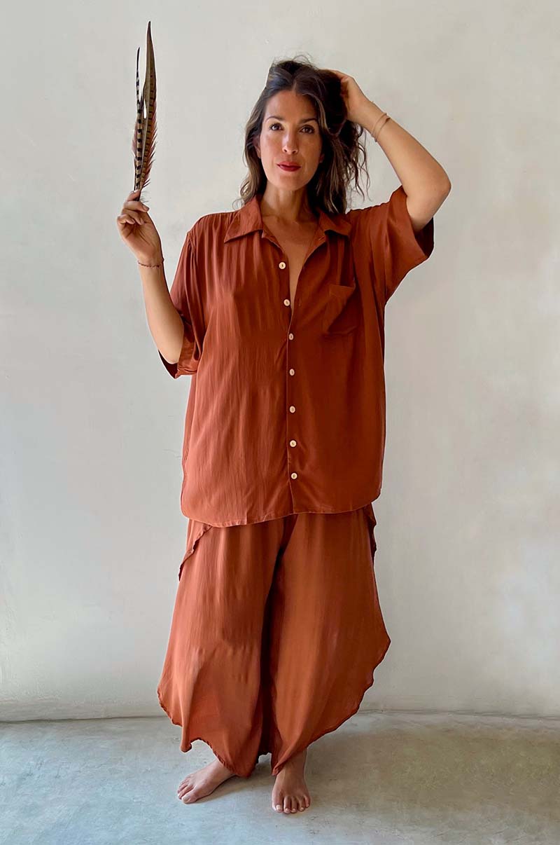 Woman wearing a rust-colored outfit holding a feather against a plain background