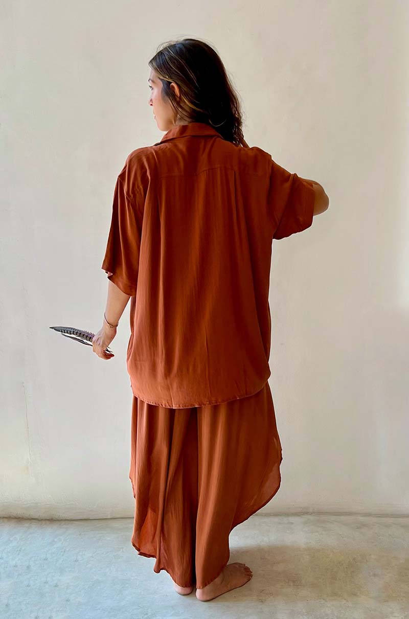 Person wearing a rust-colored outfit standing against a plain white wall.