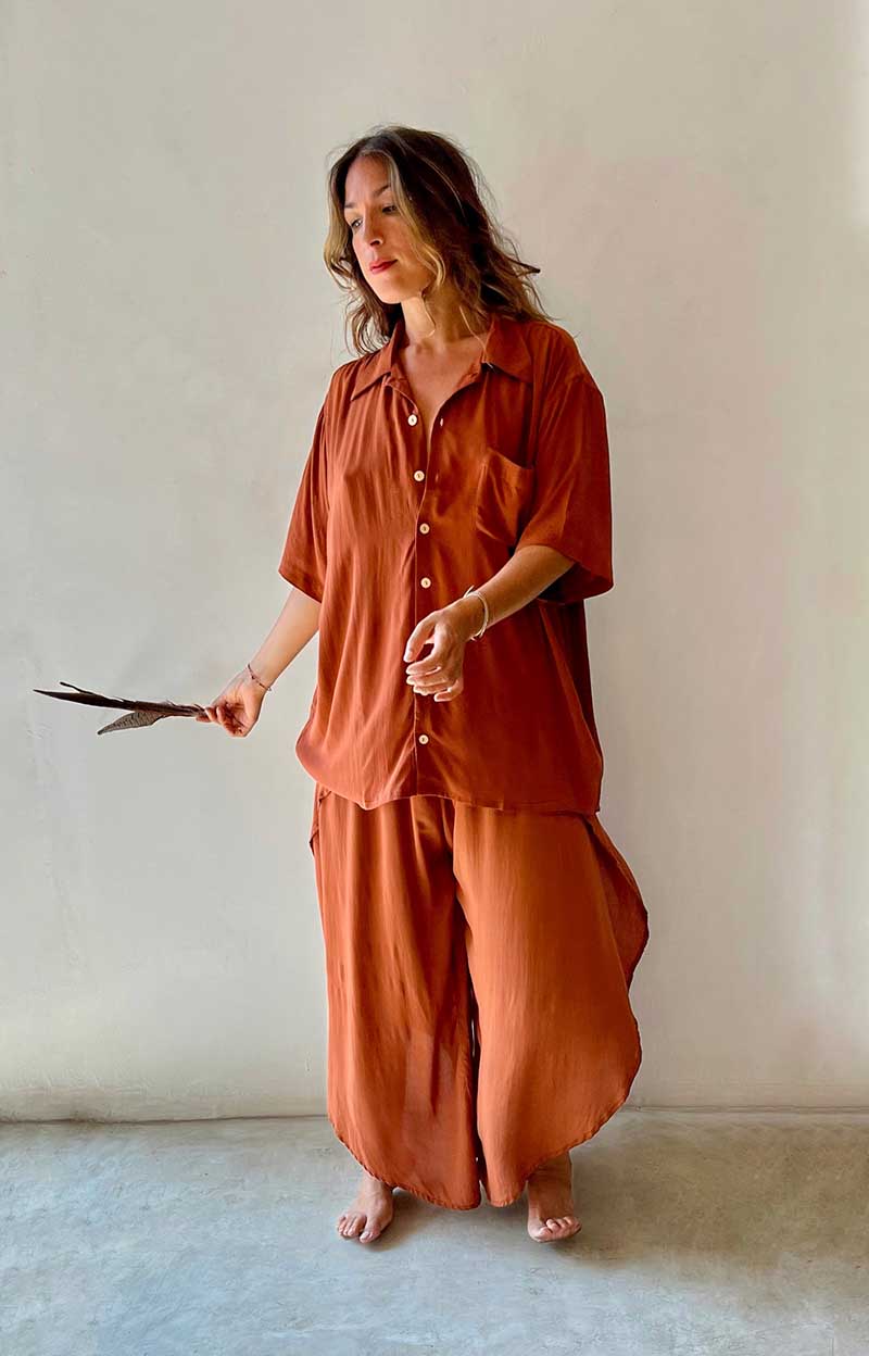 Woman wearing a rust-colored outfit holding a pair of scissors against a plain background