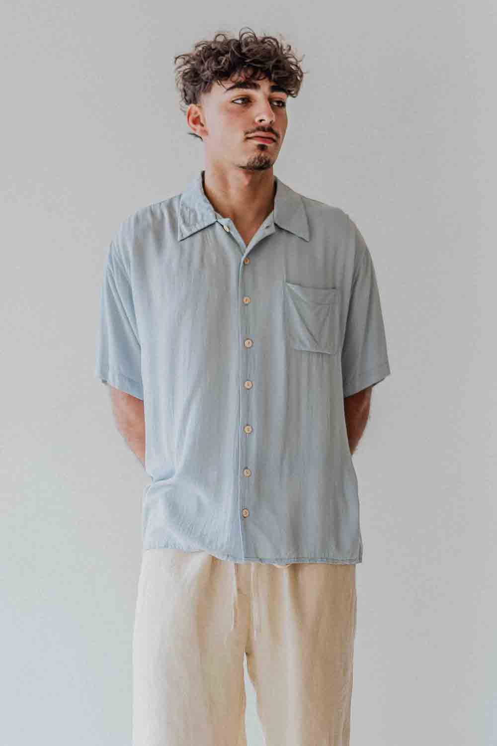Man wearing a light blue button-up shirt and beige pants against a plain background
