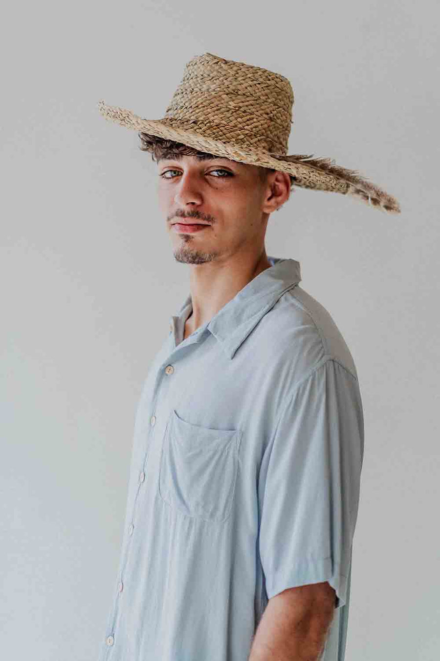 Man wearing a light blue shirt and straw hat against a plain background