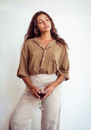 Woman wearing a brown blouse and striped pants holding a glass against a white background