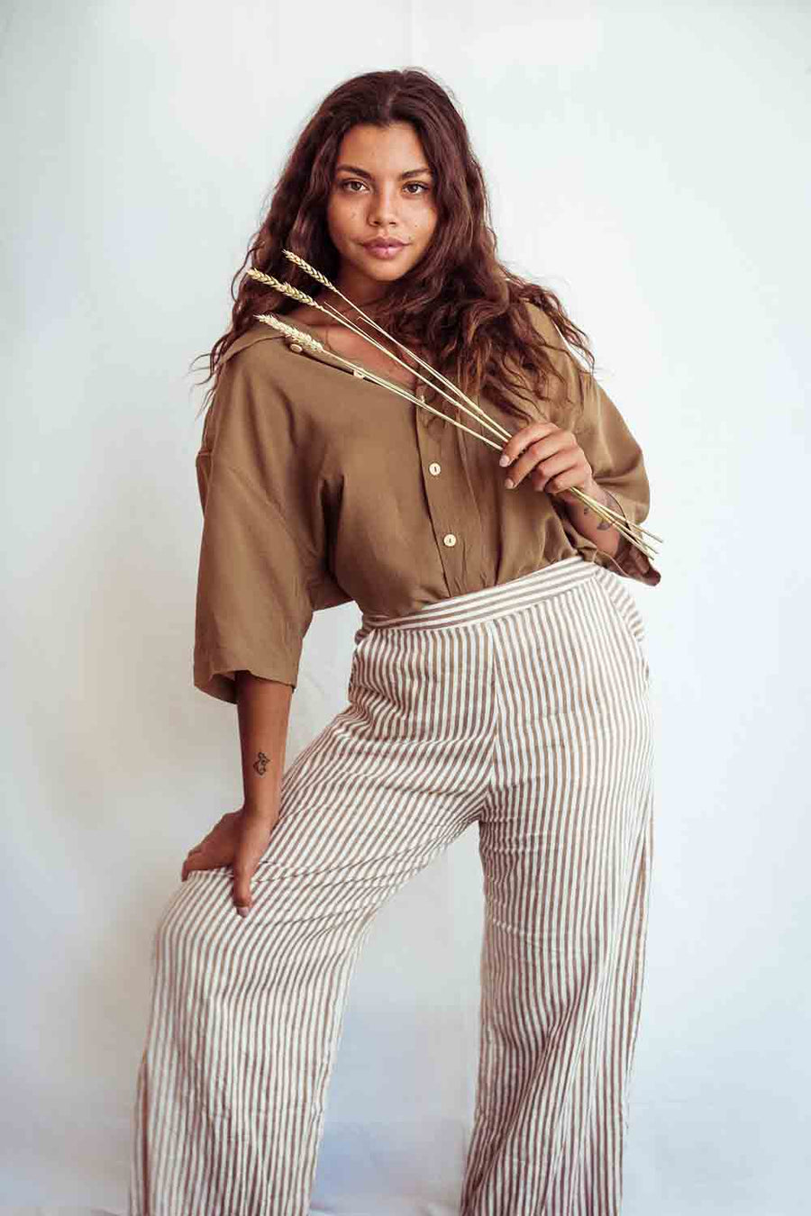 Woman wearing a brown shirt and striped pants holding a bow and arrow against a white background