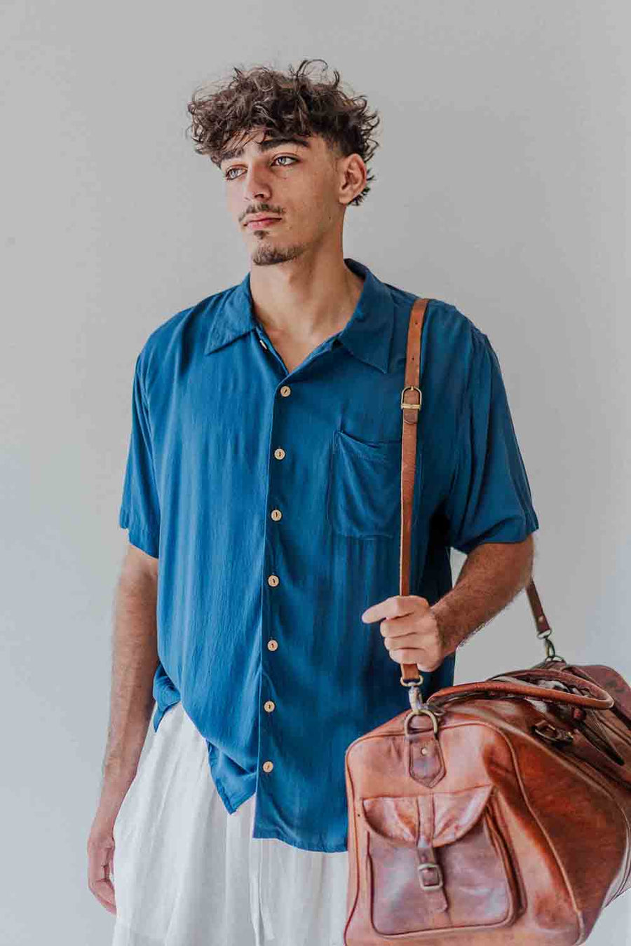 Man holding a brown leather bag against a plain background