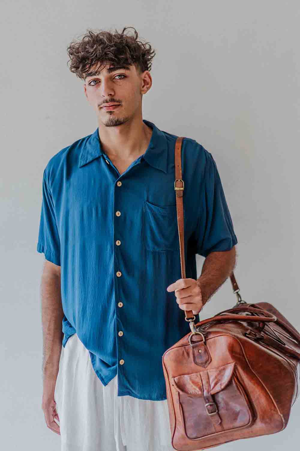 Man holding a brown leather bag against a plain background