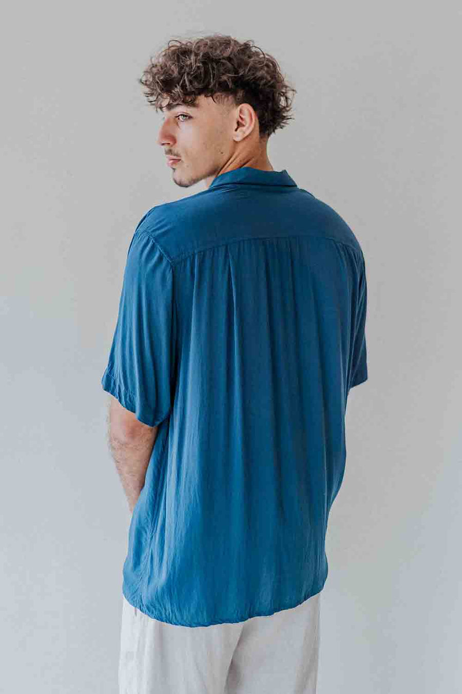 Man wearing a blue shirt and white pants against a plain background