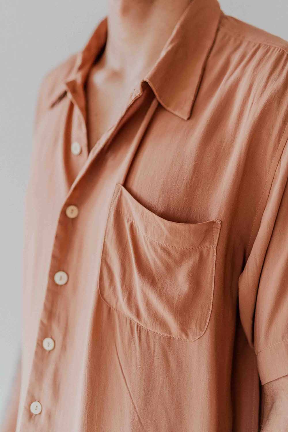 Close-up of a brown button-up shirt with a pocket on a plain background