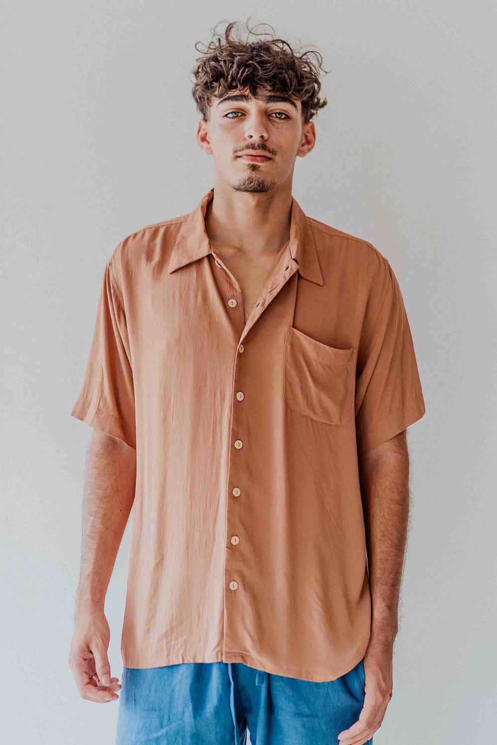 Man wearing a brown button-up shirt with a pocket on a plain background