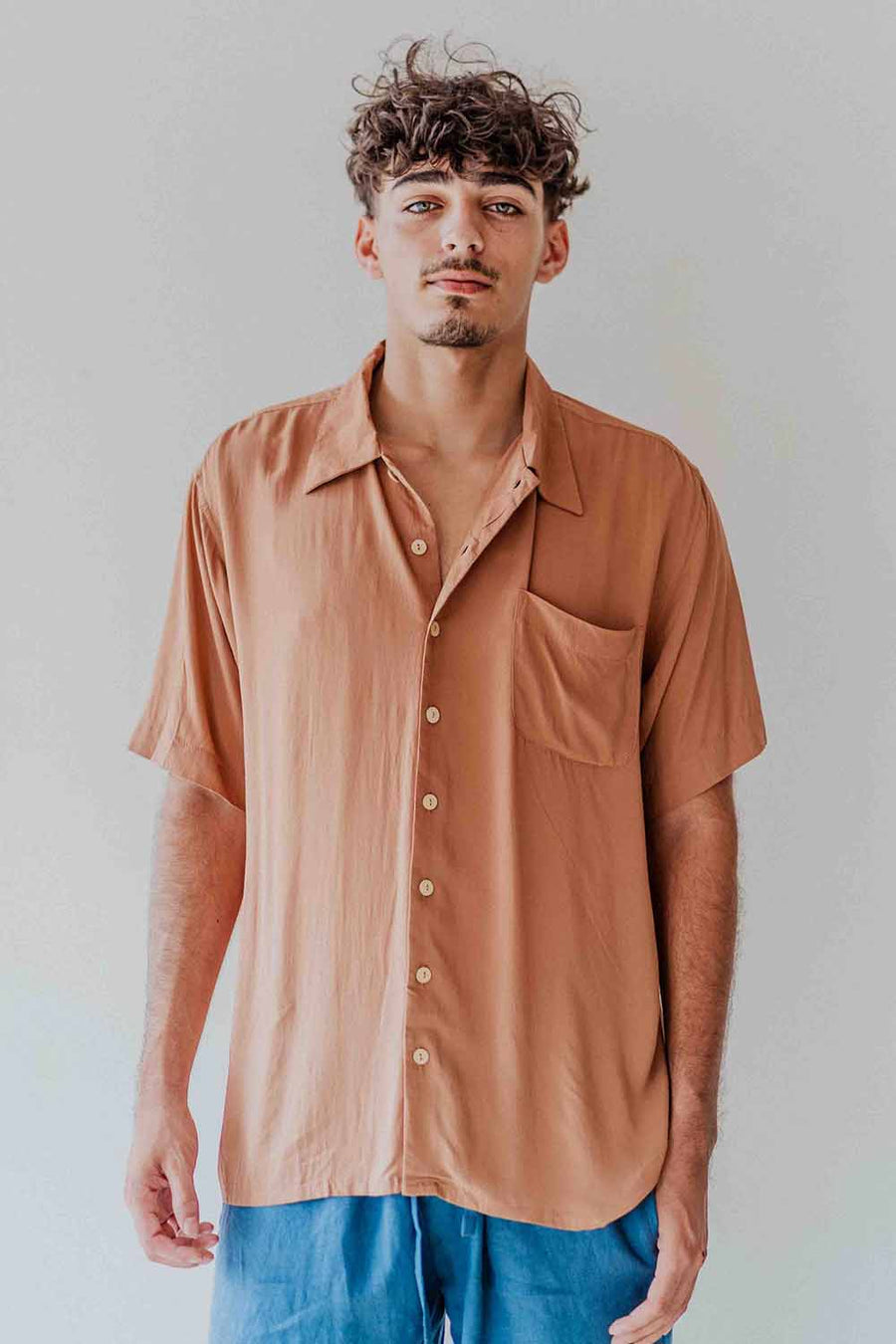 Man wearing a brown button-up shirt with a pocket on a plain background