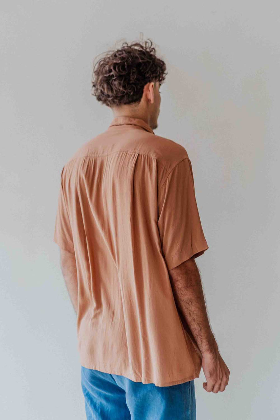 Person wearing a brown shirt and blue pants against a plain background