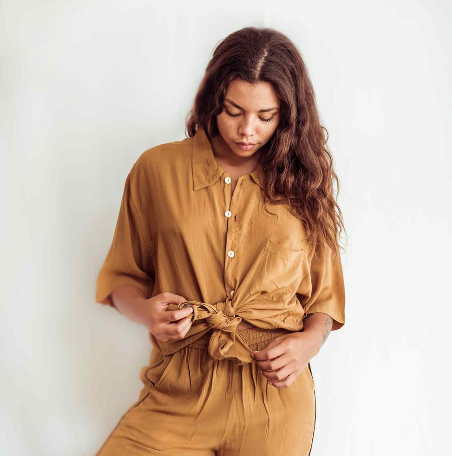 Woman wearing a mustard yellow dress with a tied waist against a plain background