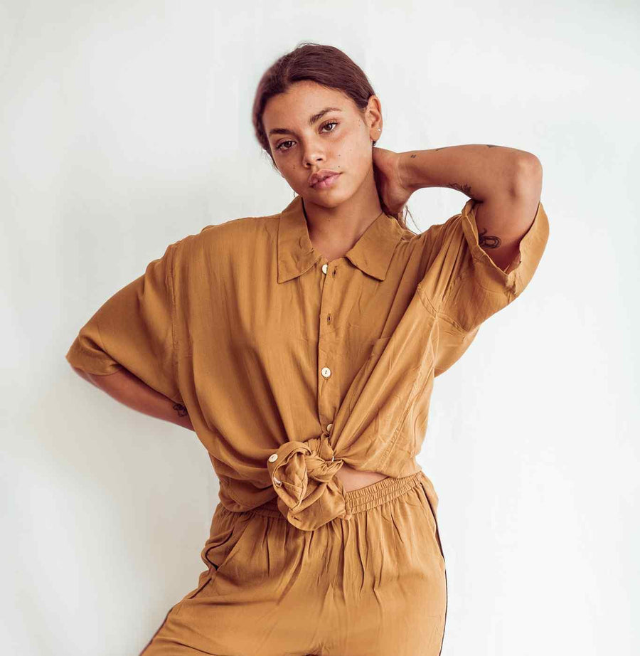 Woman wearing a mustard yellow dress with a tied waist against a plain background