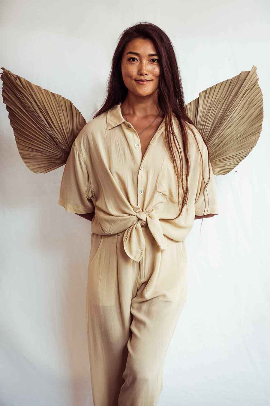 Woman wearing a beige jumpsuit with decorative wings against a white background