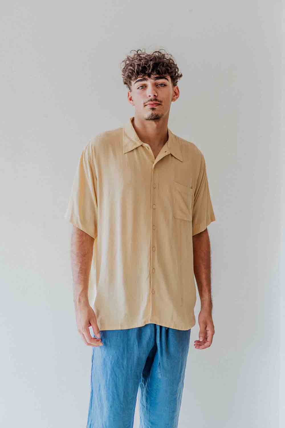 Man wearing a beige shirt and blue pants against a white background