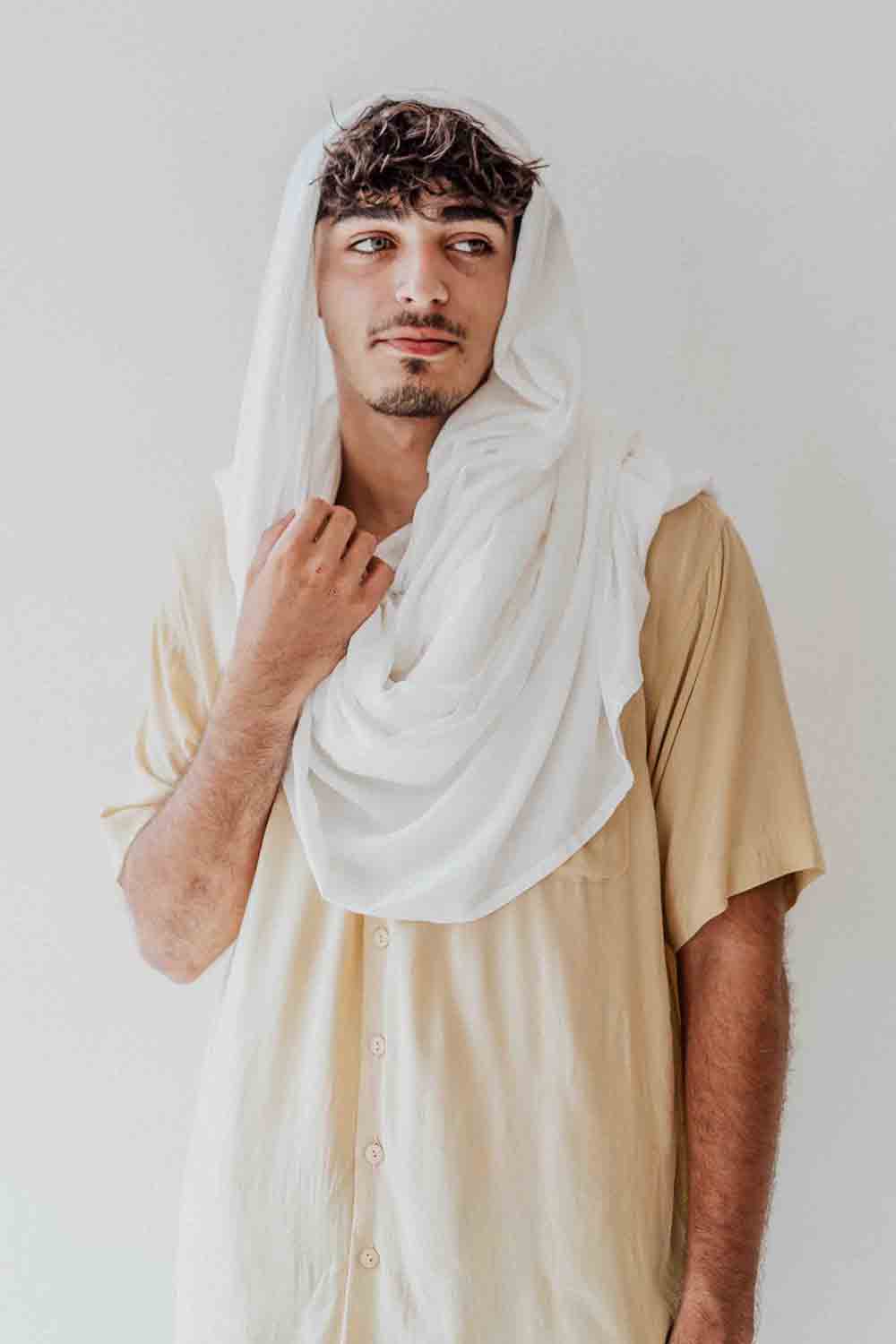 Man wearing a white headscarf and beige shirt against a plain background