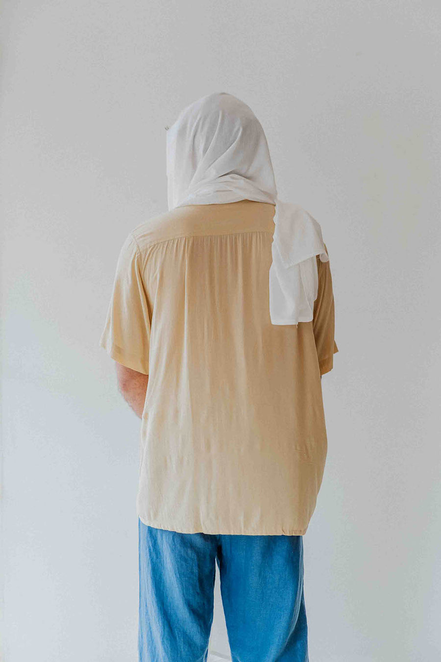 Person wearing a beige shirt and blue pants with a white hijab on a plain background