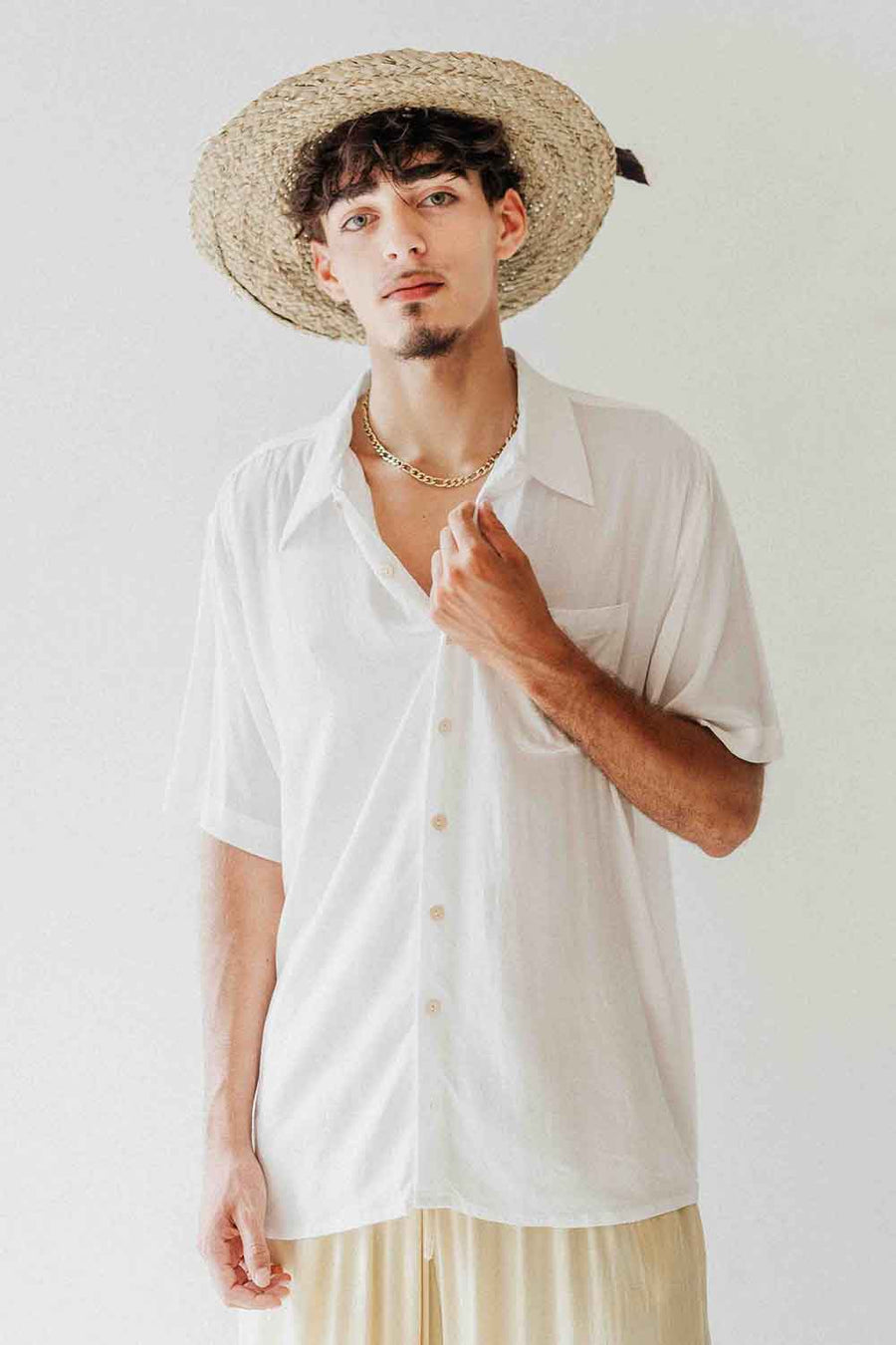 Man wearing a white shirt and straw hat against a plain background