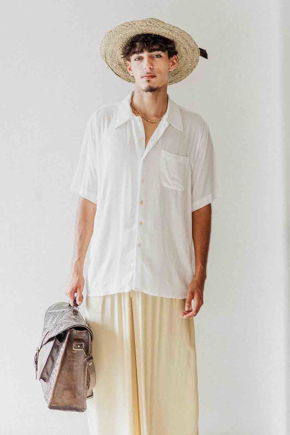 Man wearing a white shirt, beige pants, and a straw hat against a plain background