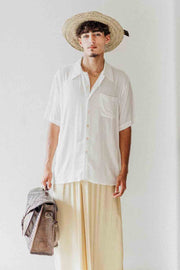 Man wearing a white shirt, beige pants, and a straw hat against a plain background