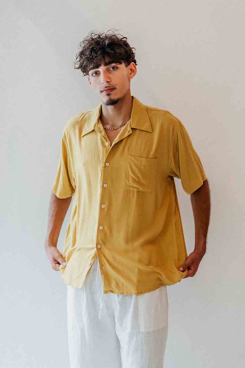 Man wearing a mustard yellow shirt and white pants against a plain background