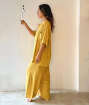 Woman wearing a mustard yellow outfit standing against a plain wall.