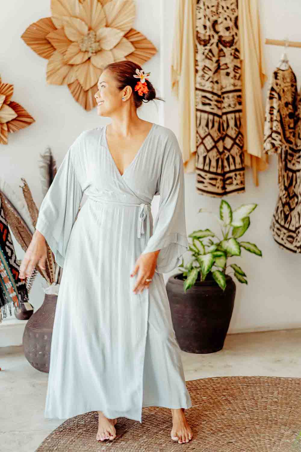 Woman in a light blue dress standing in a room with decorative elements and plants.