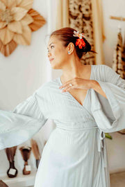 Woman in a light blue dress with a floral hair accessory in a room with decorative elements.