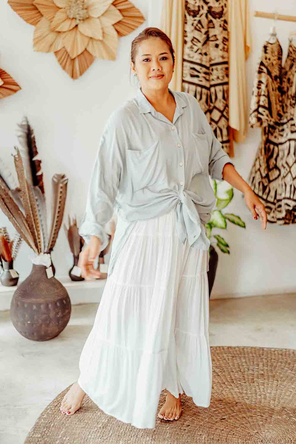 Woman in a light blue shirt and white skirt standing in a room with decorative items.