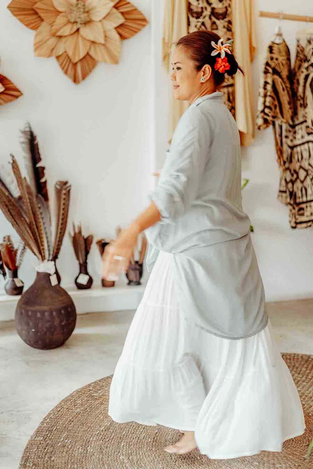 Woman in a light gray top and white skirt standing in a room with decorative elements.