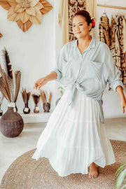 Woman in a light blue shirt and white skirt standing in a room with decorative items on the wall.