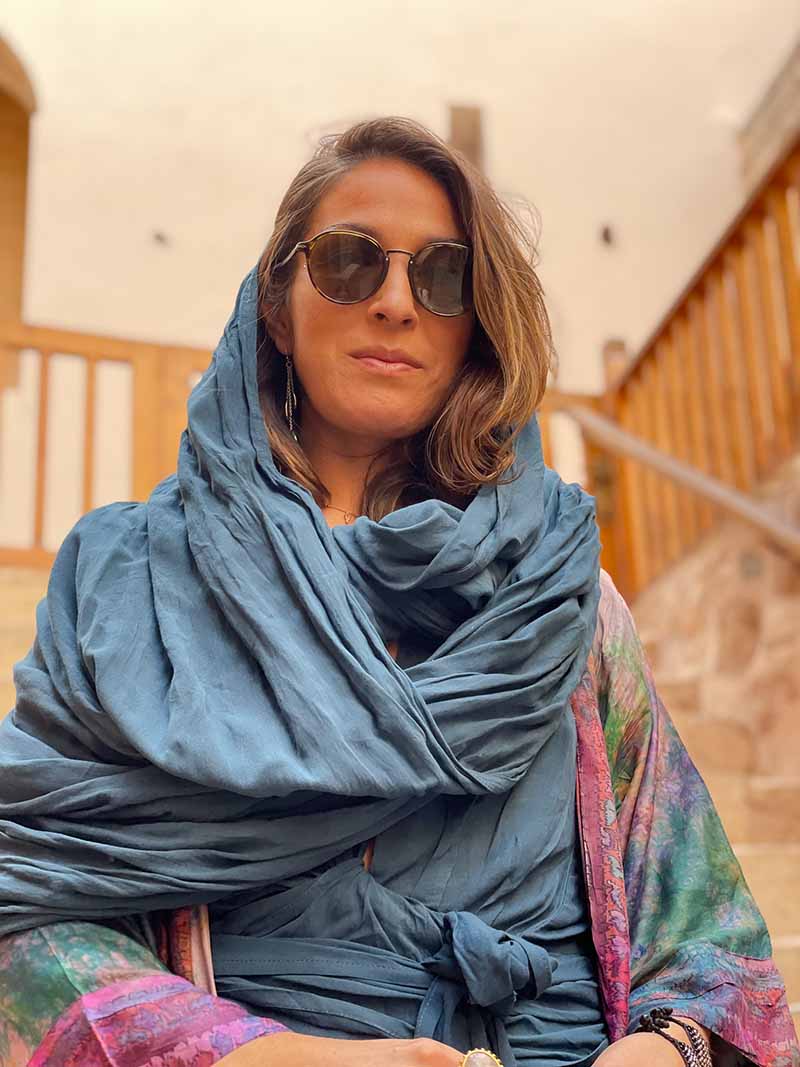 Woman wearing a blue scarf and sunglasses in an indoor setting