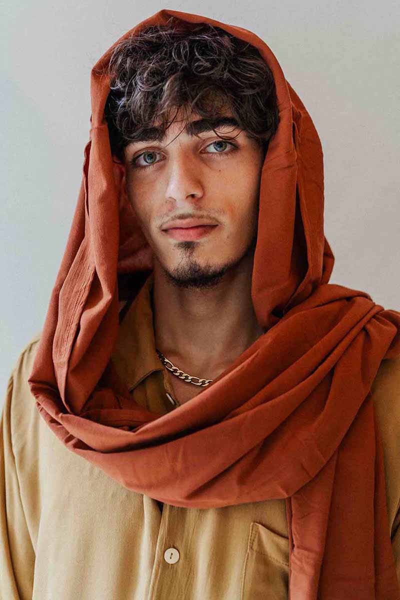 Man wearing a brown scarf and beige shirt against a plain background