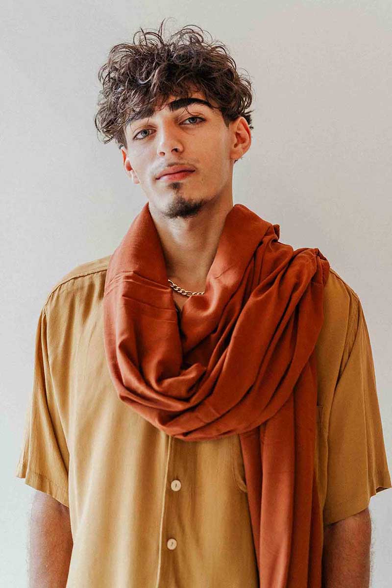 Man wearing a rust-colored scarf over a beige shirt against a plain background