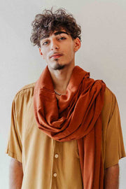Man wearing a rust-colored scarf over a beige shirt against a plain background