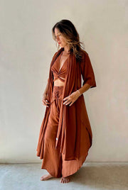 Woman wearing a rust-colored outfit with a long duster against a plain background