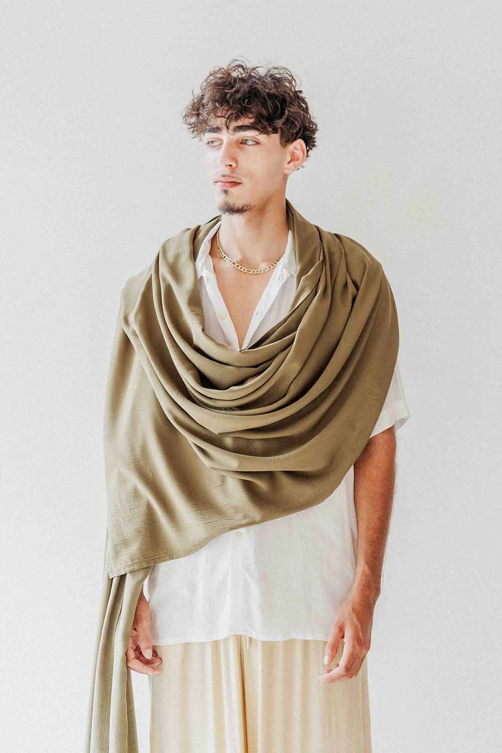 Man wearing a green shawl over a white shirt and beige pants on a plain background