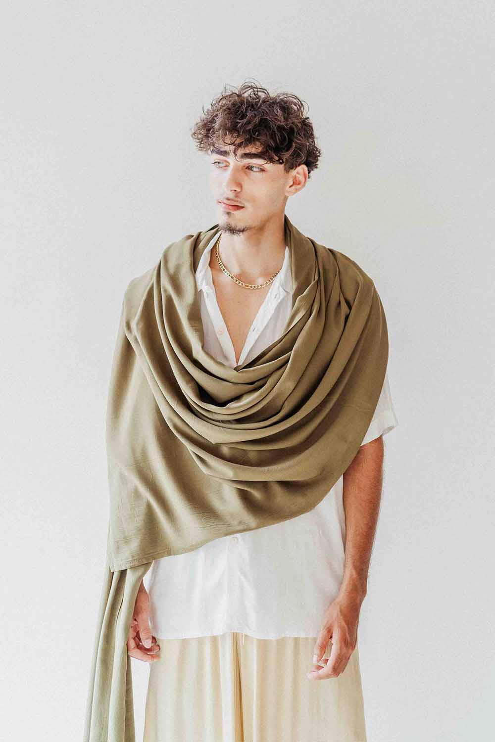 Man wearing a large green shawl over a white shirt against a plain background