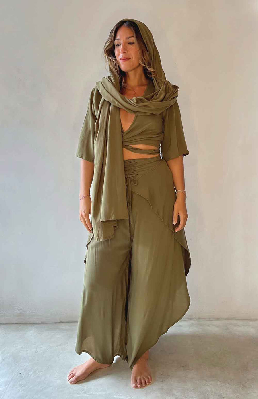 Woman wearing an olive green outfit with a scarf against a plain background