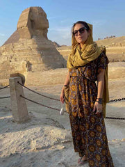 Woman in a patterned dress and yellow headscarf standing in front of the Sphinx and Pyramids at Giza.