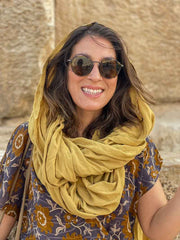 Woman wearing a yellow scarf and sunglasses with a stone wall background
