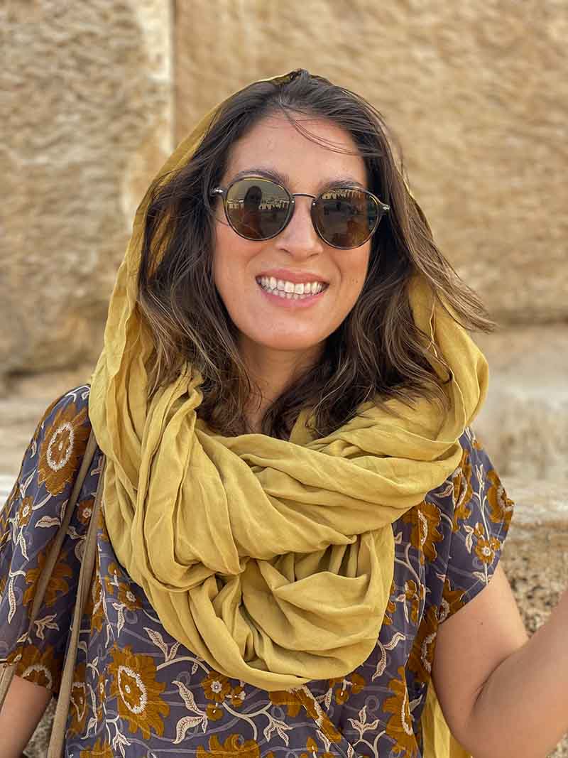 Woman wearing a yellow scarf and sunglasses with a stone wall background