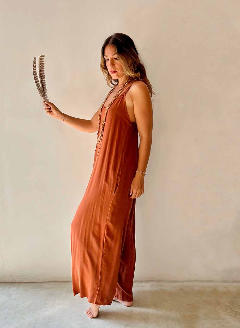 Woman in a rust-colored dress holding feathers against a neutral background