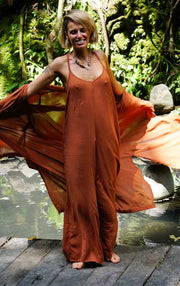 Woman in a flowing orange dress standing in a natural setting with greenery.