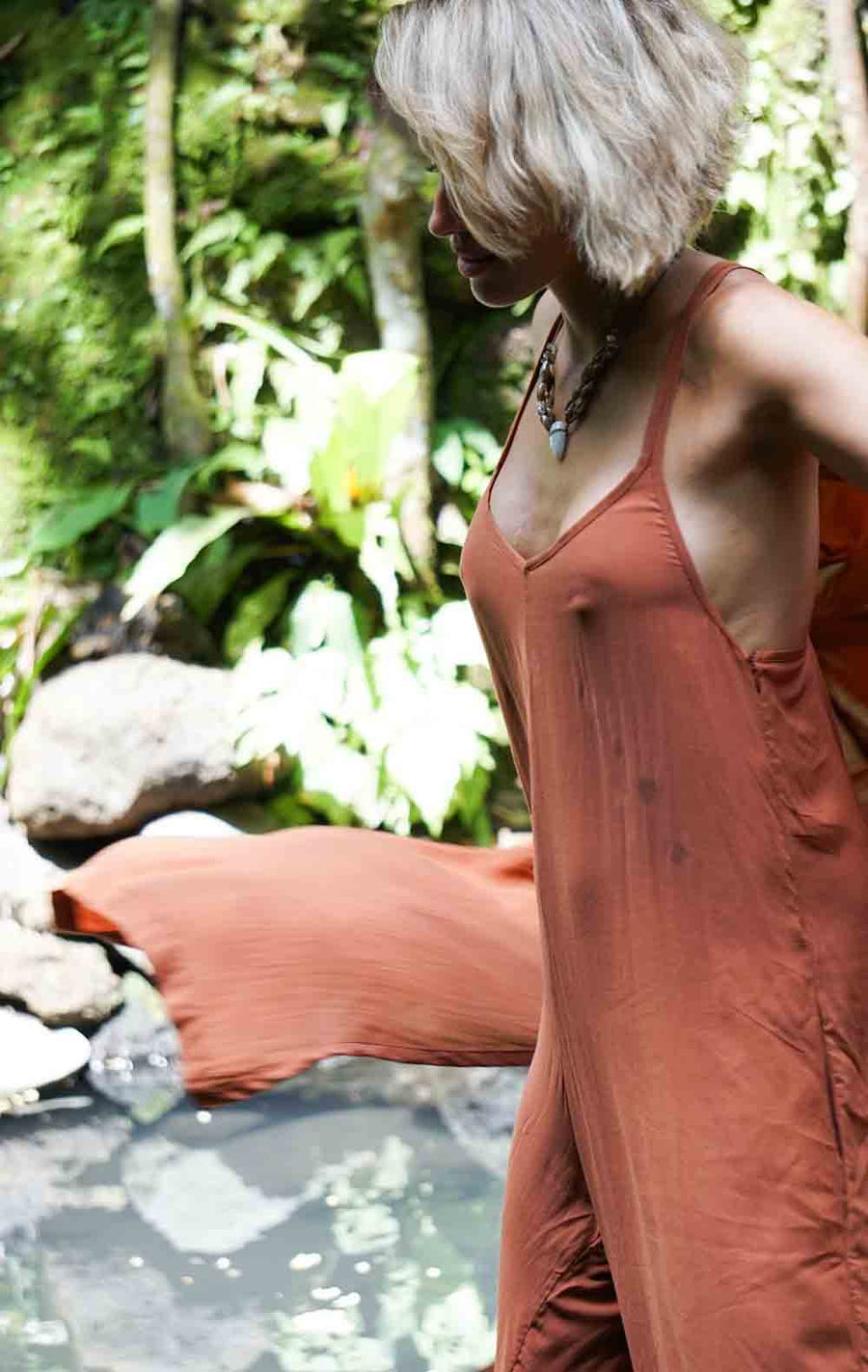 Person wearing a rust-colored dress standing in a natural setting with greenery.