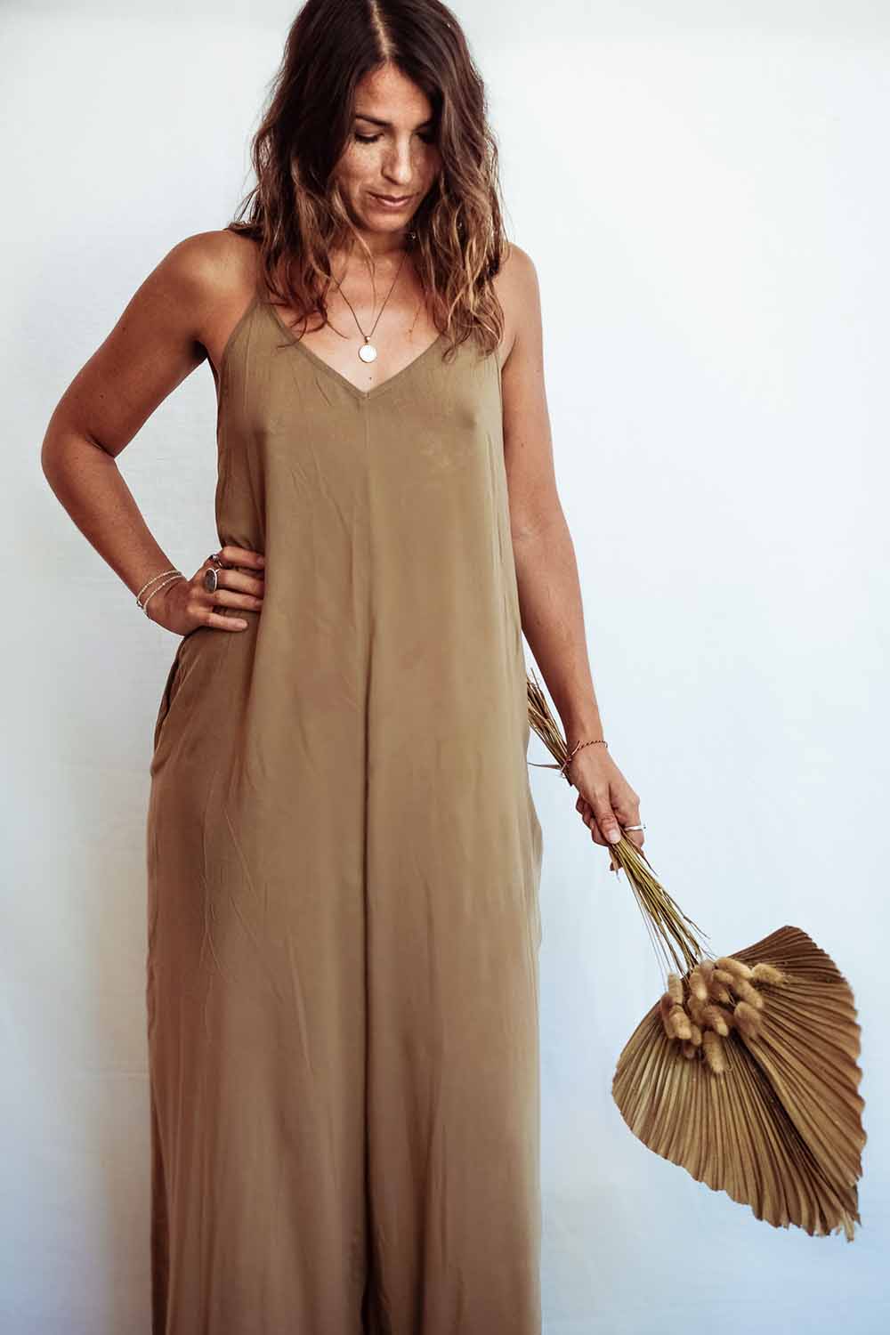 Woman wearing a brown jumpsuit holding a matching handbag against a white background