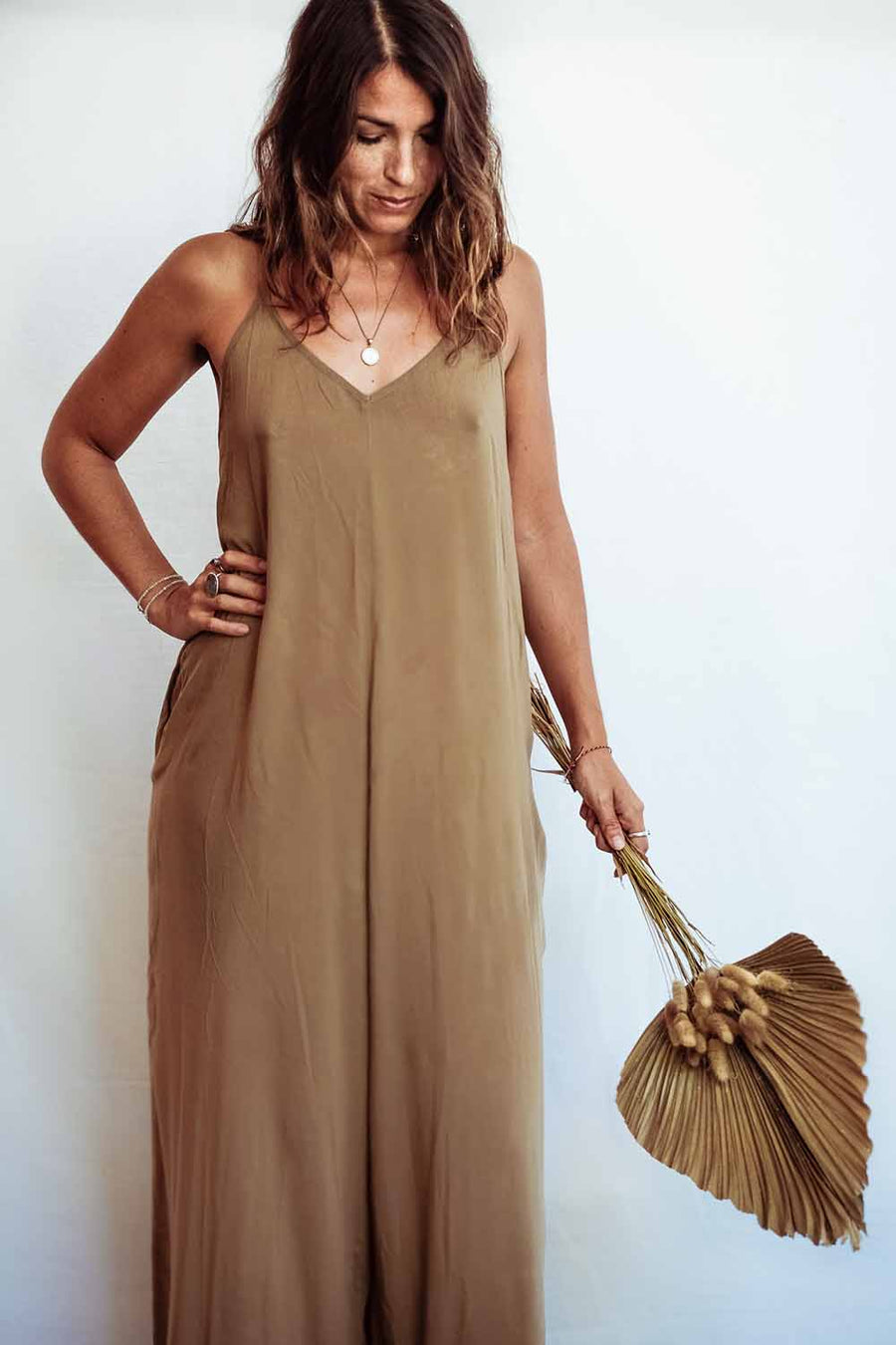 Woman wearing a brown jumpsuit holding a matching handbag against a white background