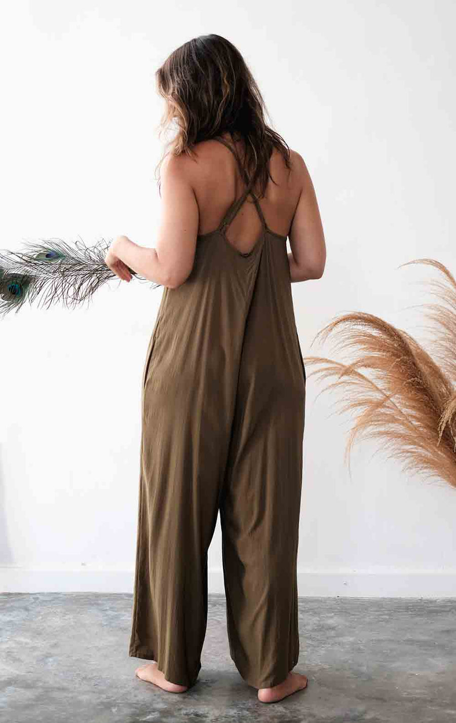 Woman wearing a green jumpsuit holding dried plants against a white wall.